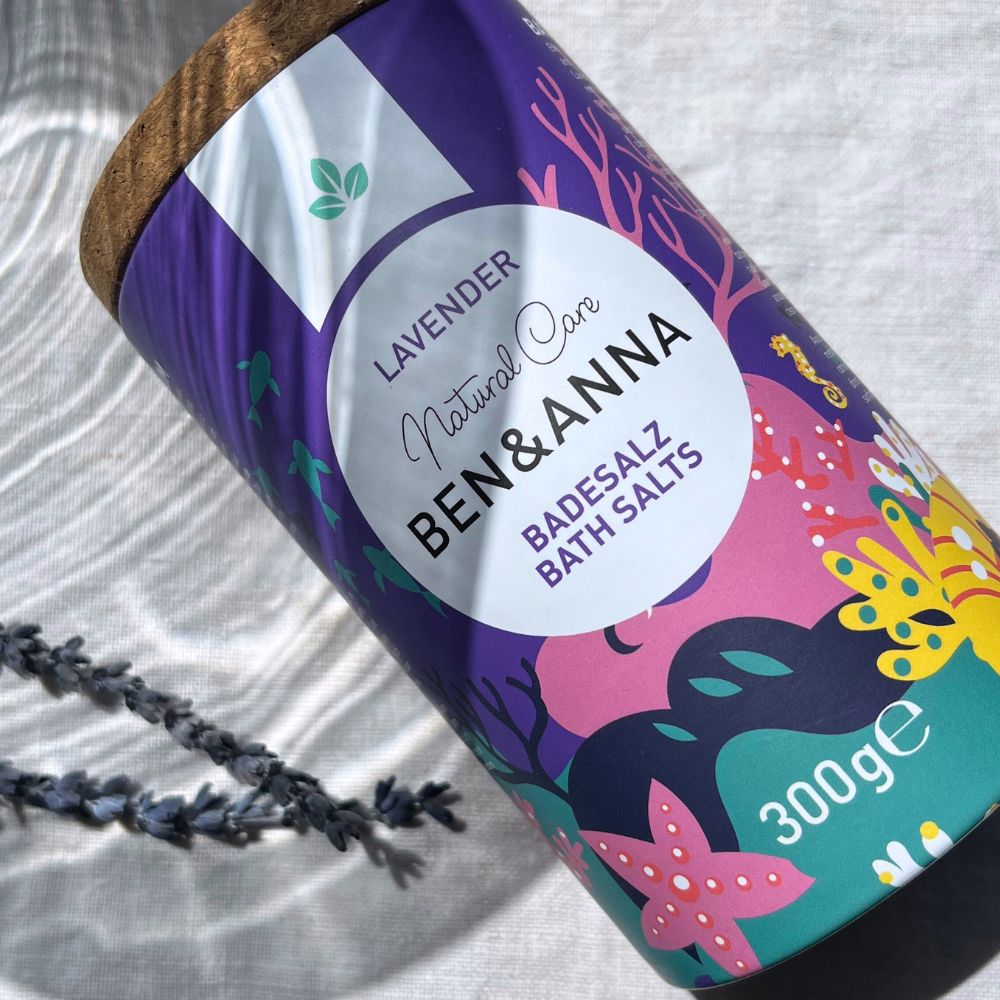 Entspanntes Badesalz mit Lavendel von BEN&ANNA in einer weißen Schüssel, mit Lavendelblüten und Duftkerzen.