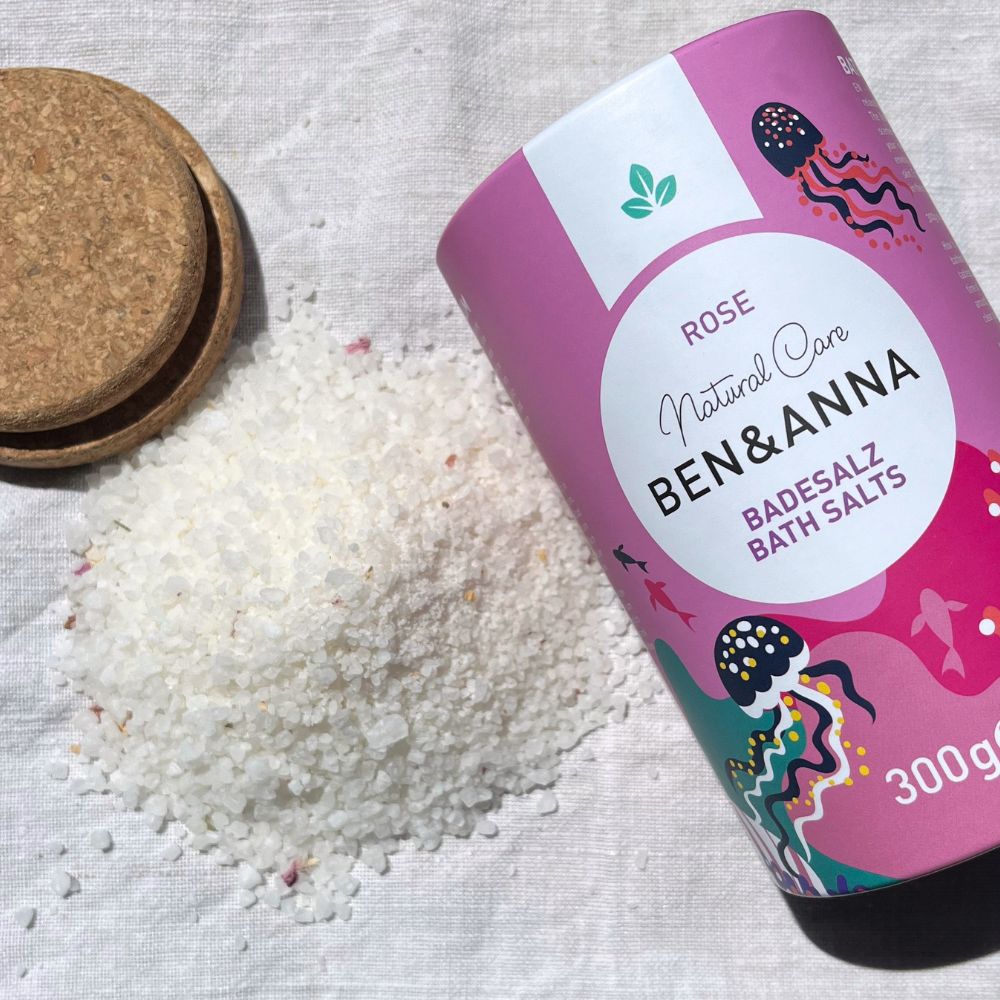 Badesalz mit Rosenaroma von BEN&ANNA, feines rosa Badesalz in einer Schale mit Blumen und Kerzen für entspannendes Bad