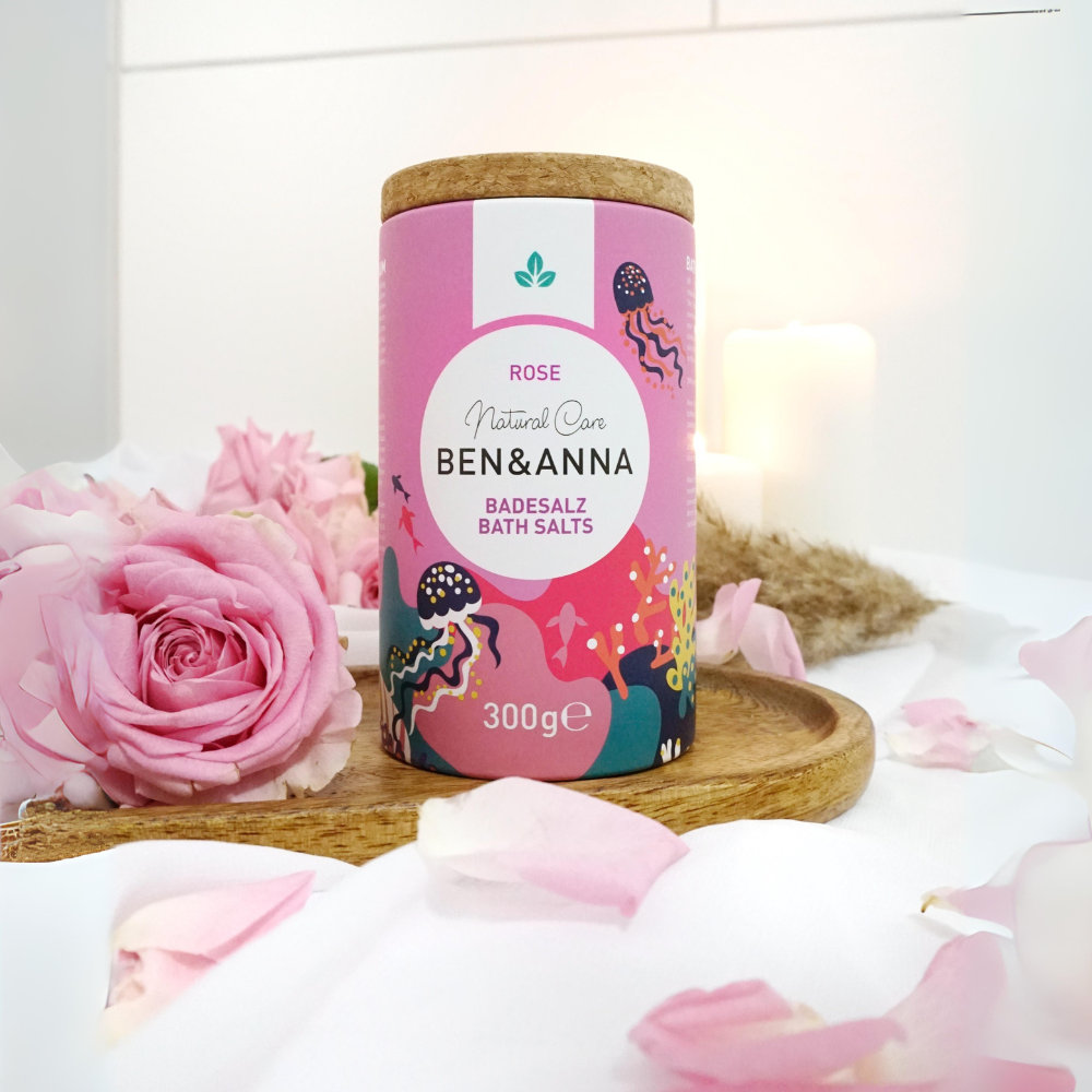 Hochwertiges Badesalz mit Rose-Duft von BEN&ANNA, zeigt eine offene Packung mit rosa Badesalz und Rosenblüten.